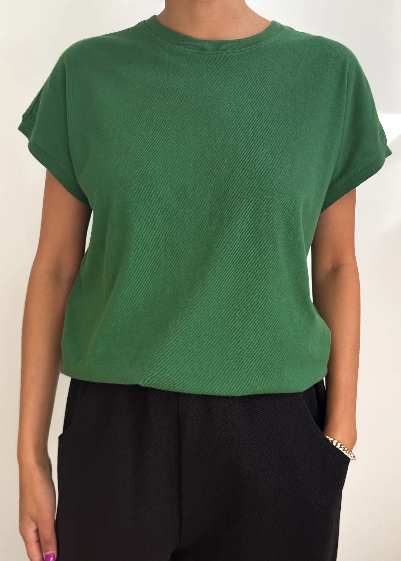 Person wearing a green t-shirt and black pants against a white background