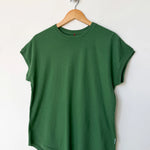 Green t-shirt on a wooden hanger against a white wall