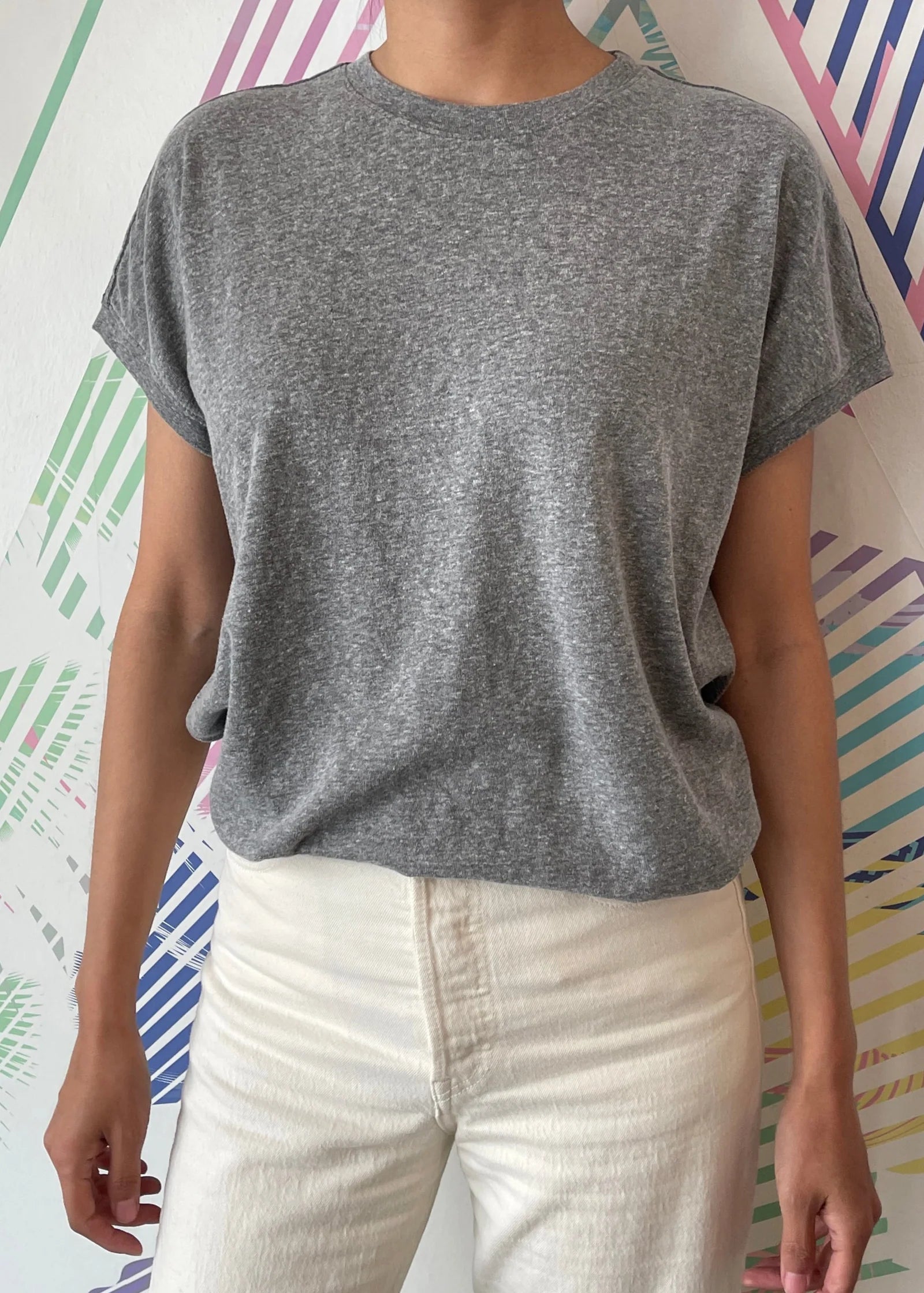 Person wearing a gray t-shirt and white pants against a colorful abstract background