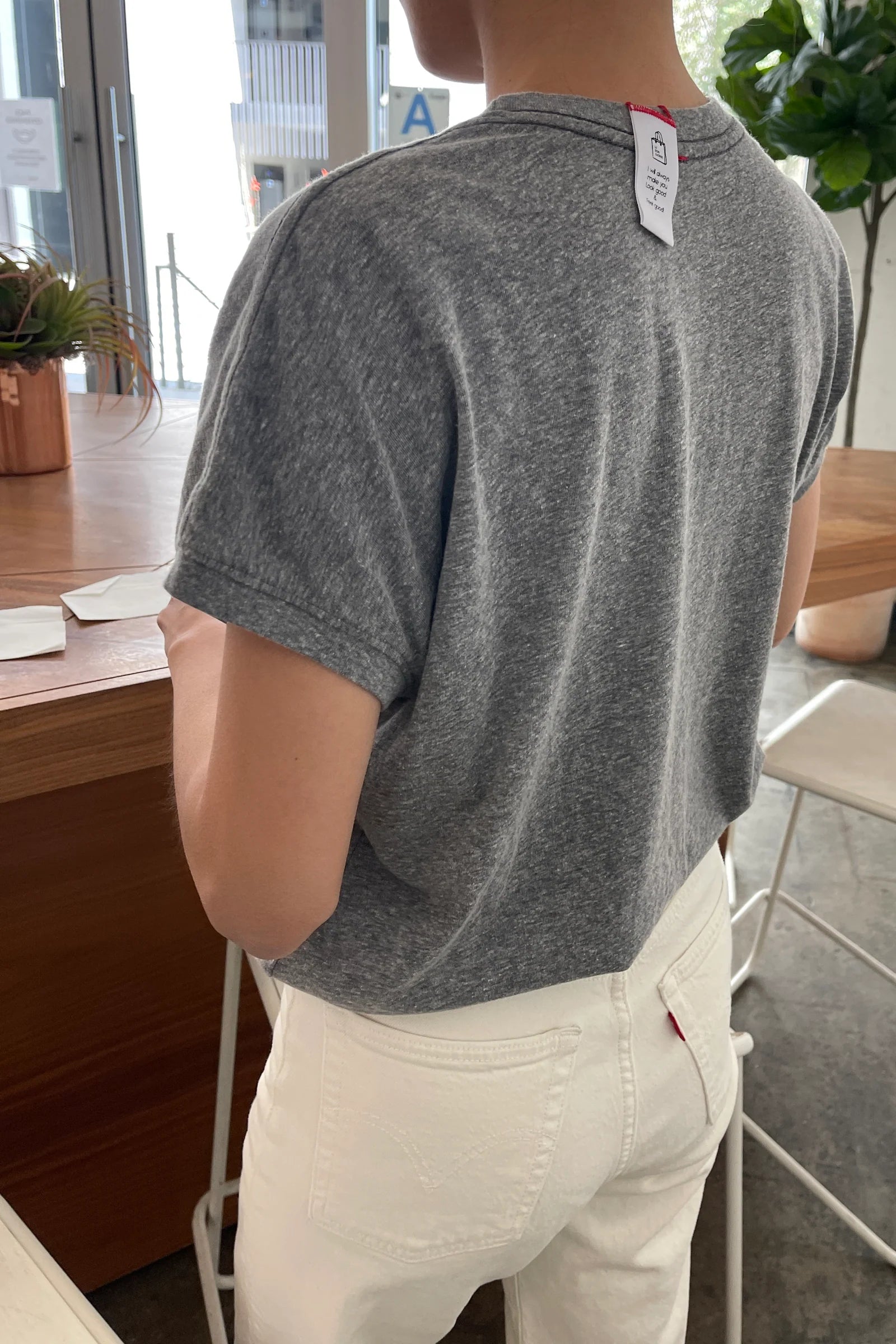 Person wearing a gray t-shirt with a brand tag in an indoor setting