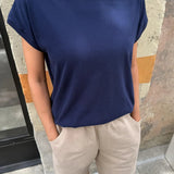 Person wearing a navy blue t-shirt and beige pants standing against a stone wall.