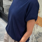 Person wearing a navy blue t-shirt and beige pants standing against a textured wall.