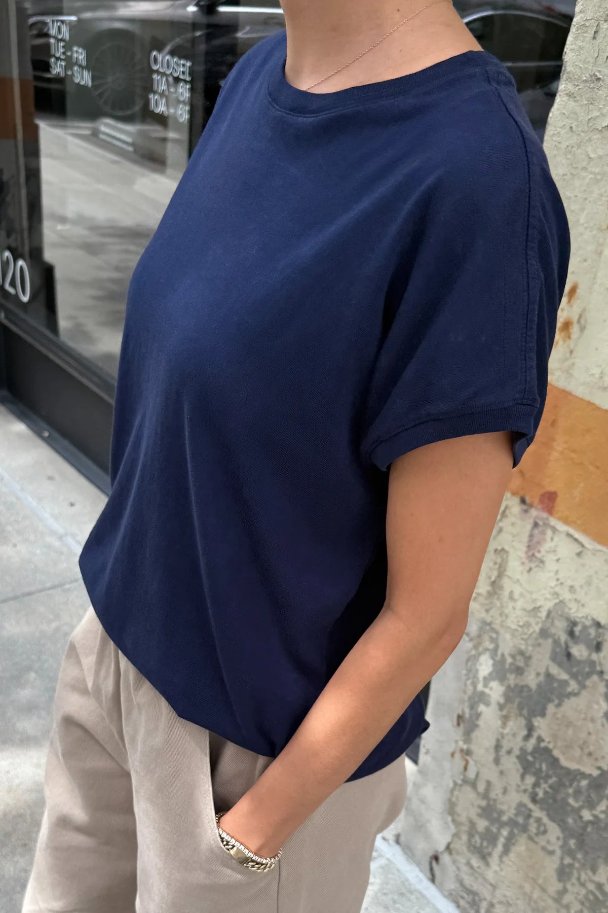 Person wearing a navy blue t-shirt and beige pants standing against a textured wall.