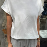 Person wearing a white t-shirt and gray pants against a textured wall.
