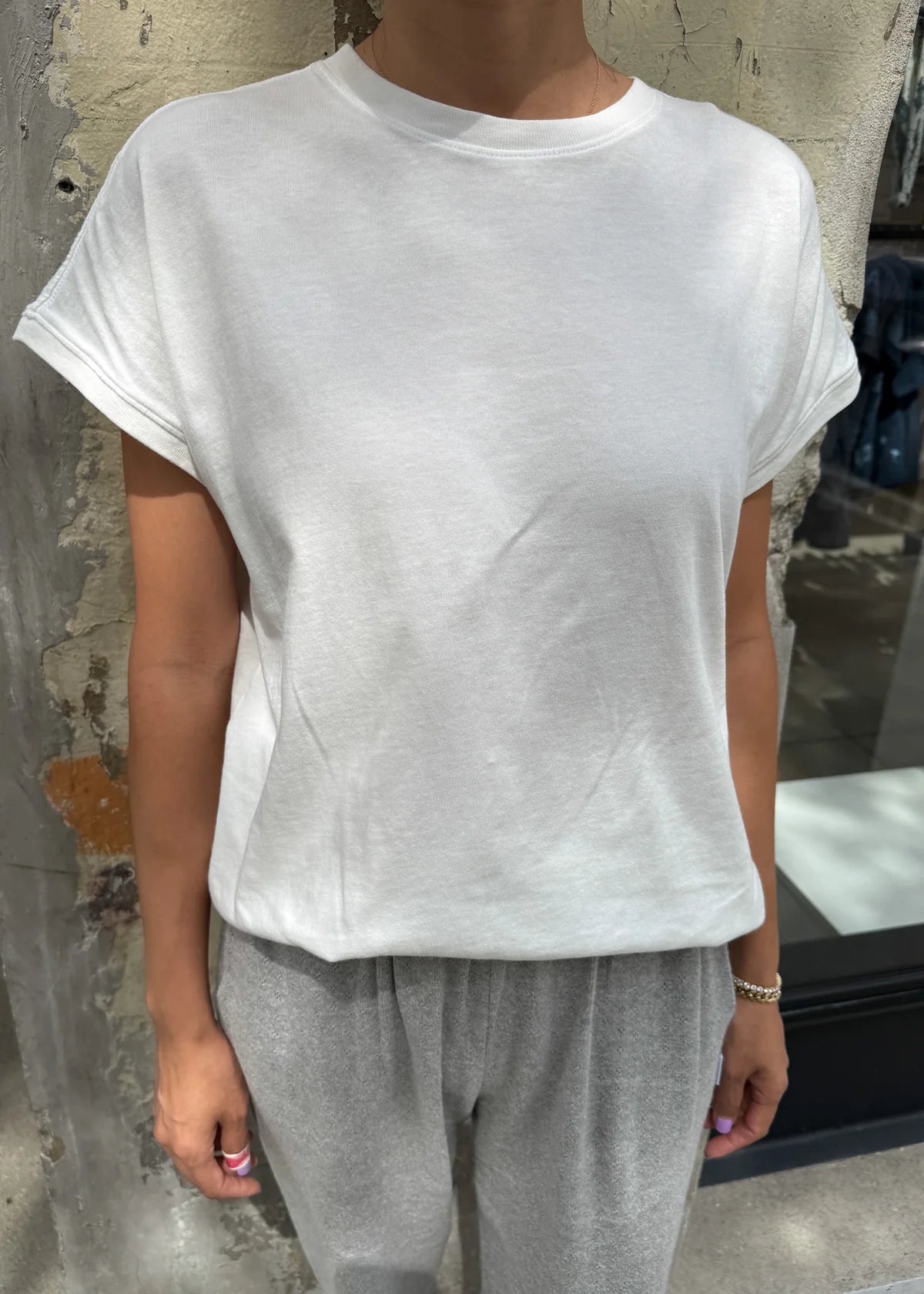 Person wearing a white t-shirt and gray pants against a textured wall.