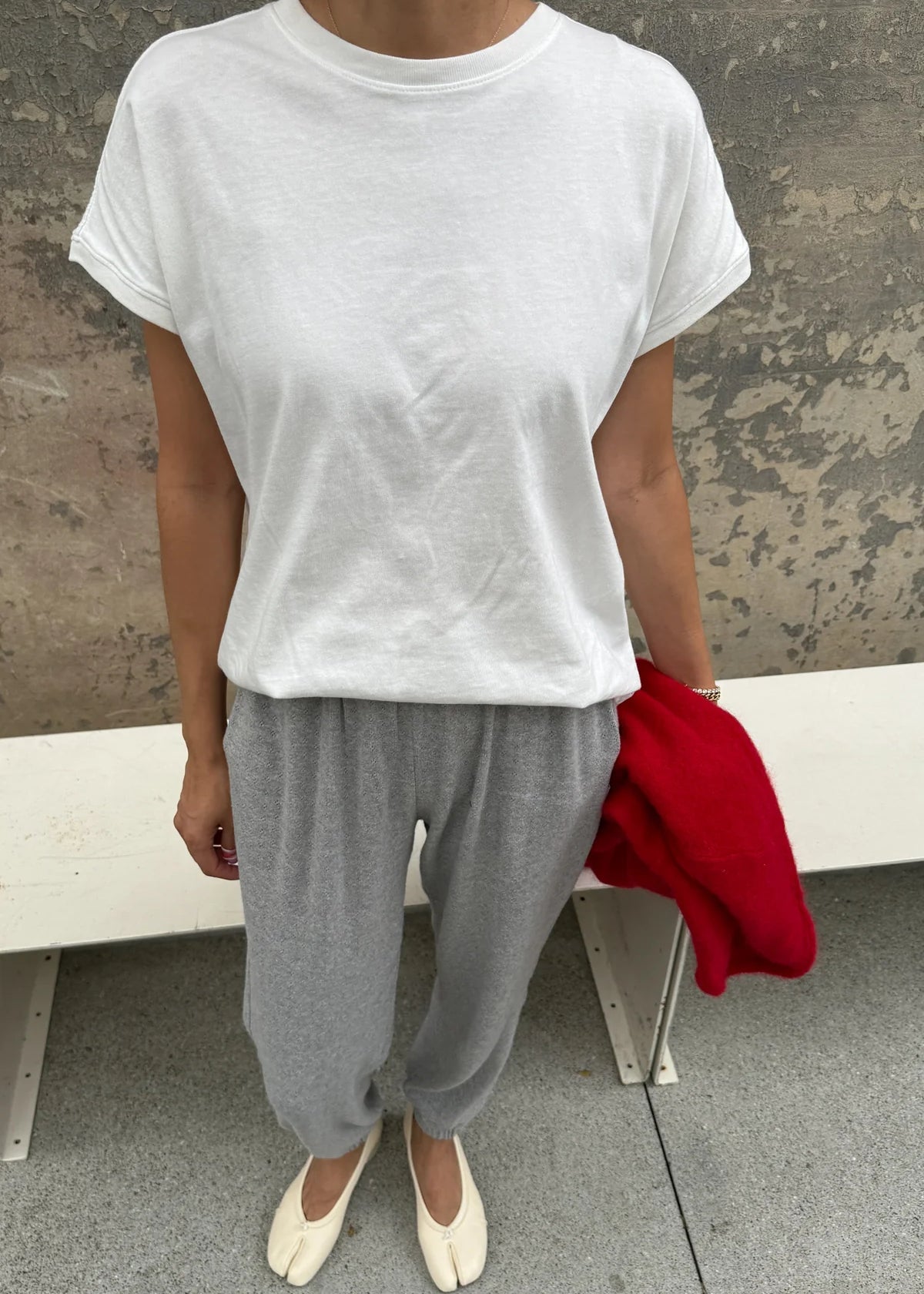 Person wearing a white t-shirt and gray pants sitting on a bench with a red jacket.