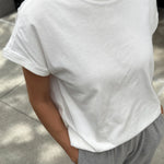 Person wearing a plain white t-shirt and gray pants on a sidewalk.