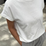 Person wearing a plain white t-shirt and gray pants on a sidewalk.