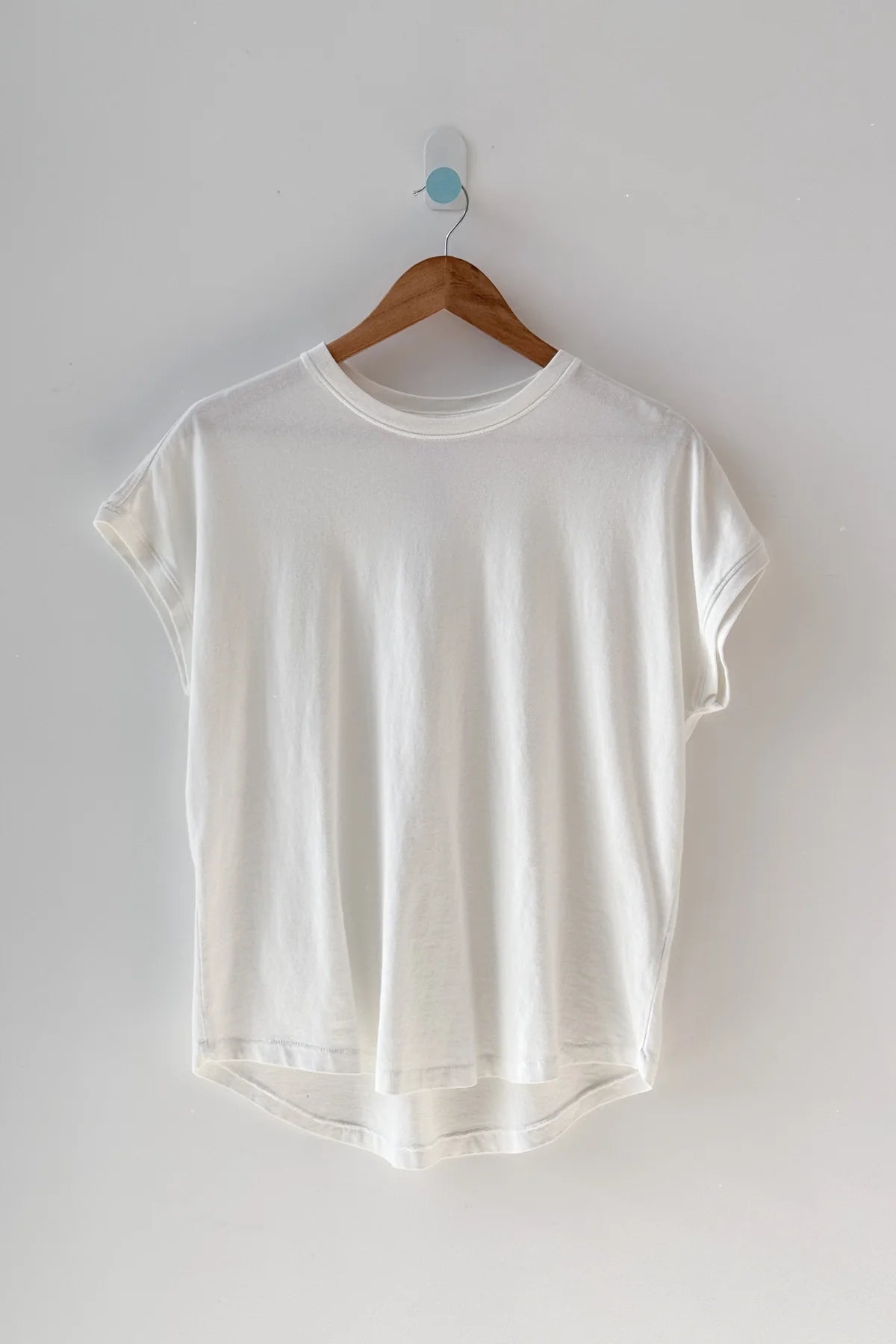 White t-shirt on a wooden hanger against a white wall