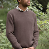 Man wearing a brown sweater standing in a forest setting