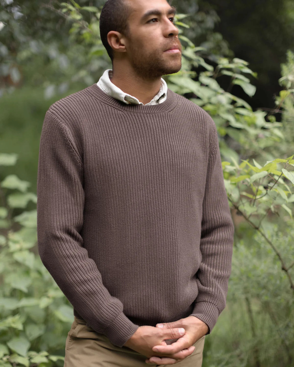 Man wearing a brown sweater standing in a forest setting