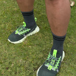 Person wearing black sneakers with green accents on grass