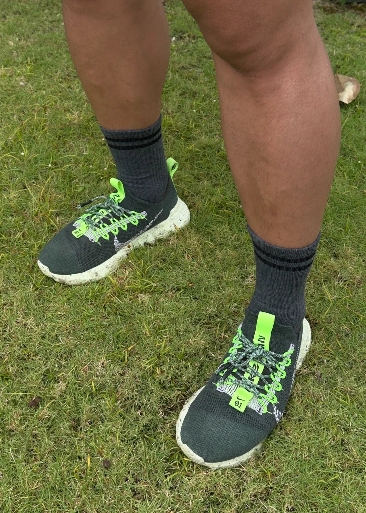 Person wearing black sneakers with green accents on grass