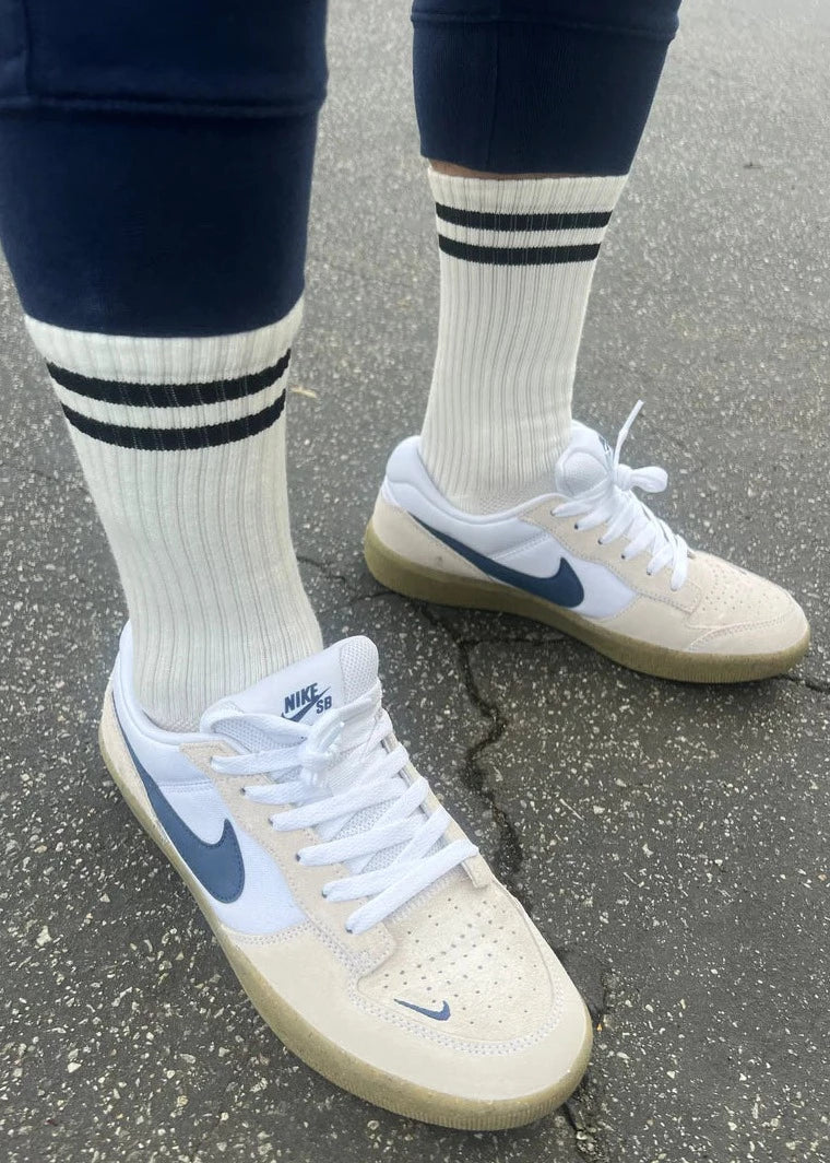 A pair of classic white socks with two black horizontal stripes near the top, worn with sneakers.