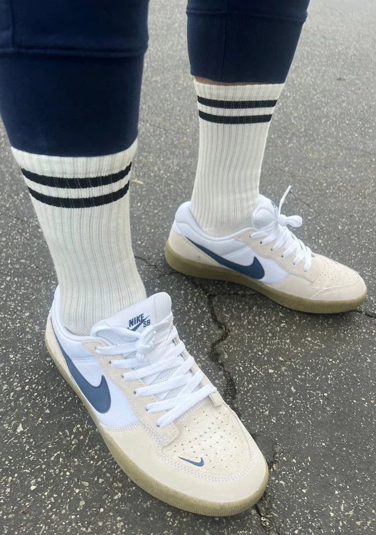 A pair of classic white socks with two black horizontal stripes near the top, worn with sneakers.