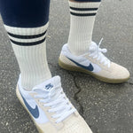 A pair of classic white socks with two black horizontal stripes near the top, worn with sneakers.