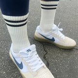A pair of classic white socks with two black horizontal stripes near the top, worn with sneakers.