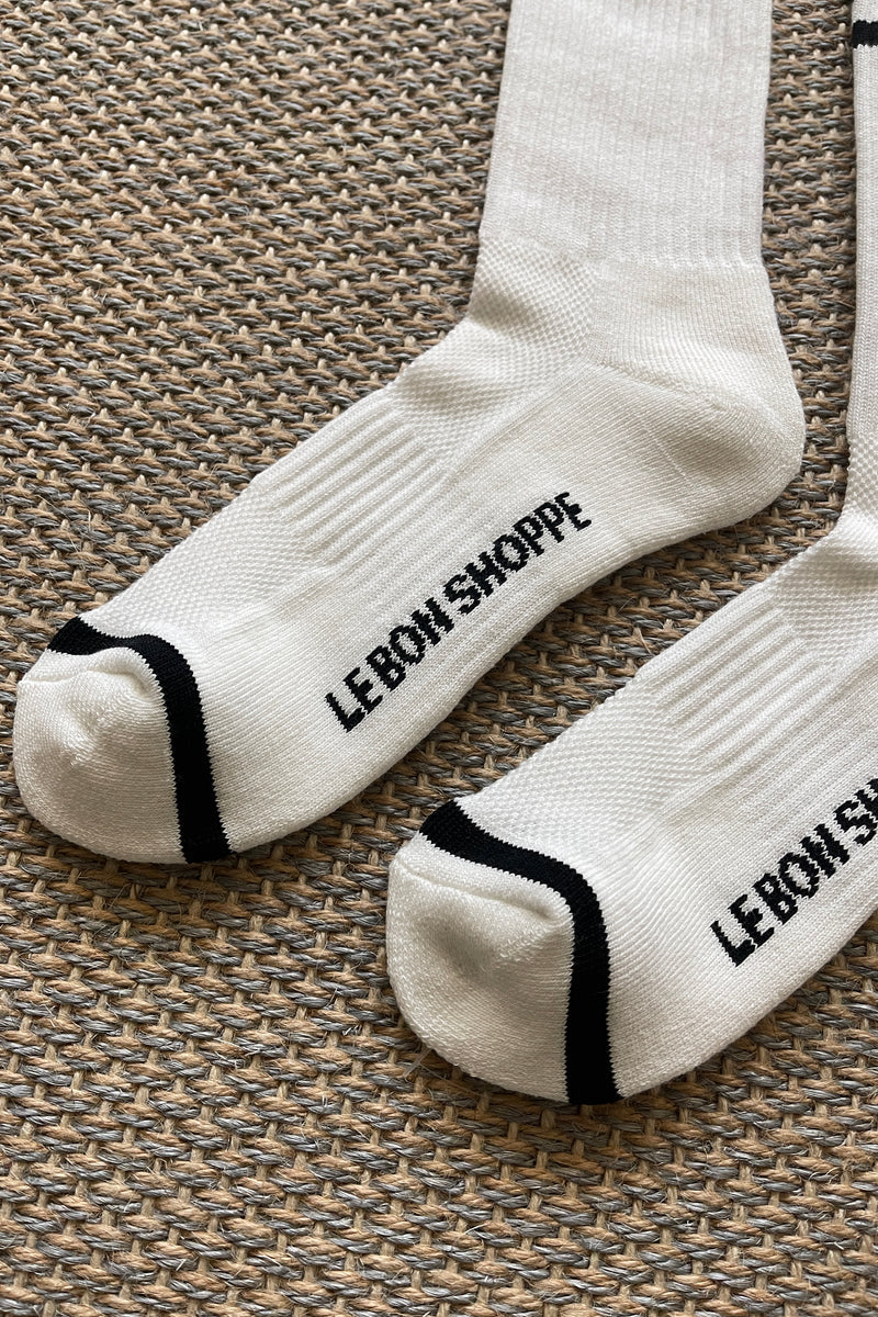 White socks with black stripes and Le Bon Shoppe branding laying on tan carpet.