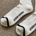 White socks with black stripes and Le Bon Shoppe branding laying on tan carpet.