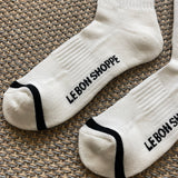White socks with black stripes and Le Bon Shoppe branding laying on tan carpet.