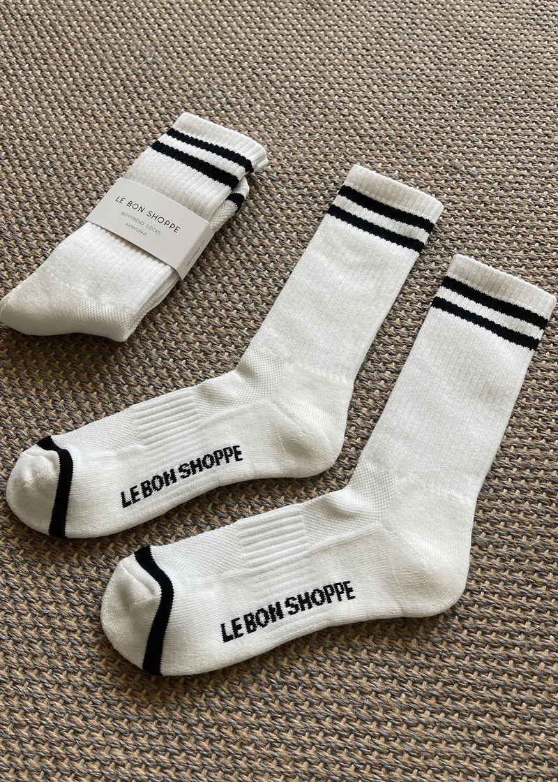 White socks with black stripes and Le Bon Shoppe branding laying on tan carpet.
