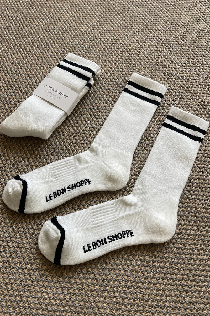 White socks with black stripes and Le Bon Shoppe branding laying on tan carpet.