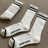 White socks with black stripes and Le Bon Shoppe branding laying on tan carpet.