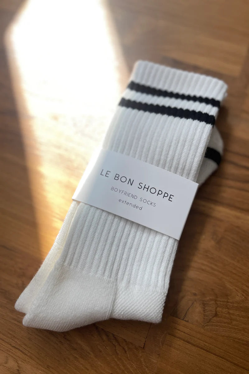 White socks with black stripes in Le Bon Shoppe packaging on wood floor.
