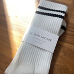 White socks with black stripes in Le Bon Shoppe packaging on wood floor.