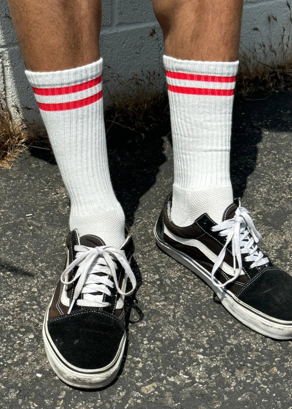 A pair of white socks with red stripes on the cuff, worn with black and white sneakers.