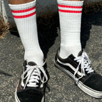 A pair of white socks with red stripes on the cuff, worn with black and white sneakers.