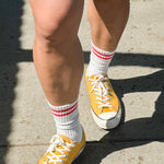 Person wearing green shorts, white socks with red stripes and yellow sneakers walking on a sidewalk.