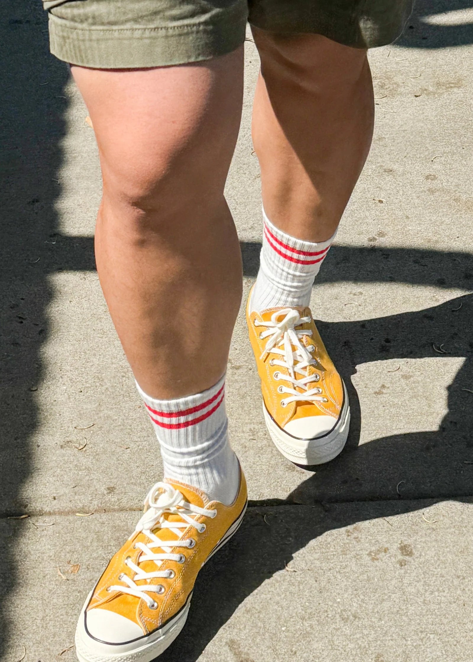 Person wearing green shorts, white socks with red stripes and yellow sneakers walking on a sidewalk.