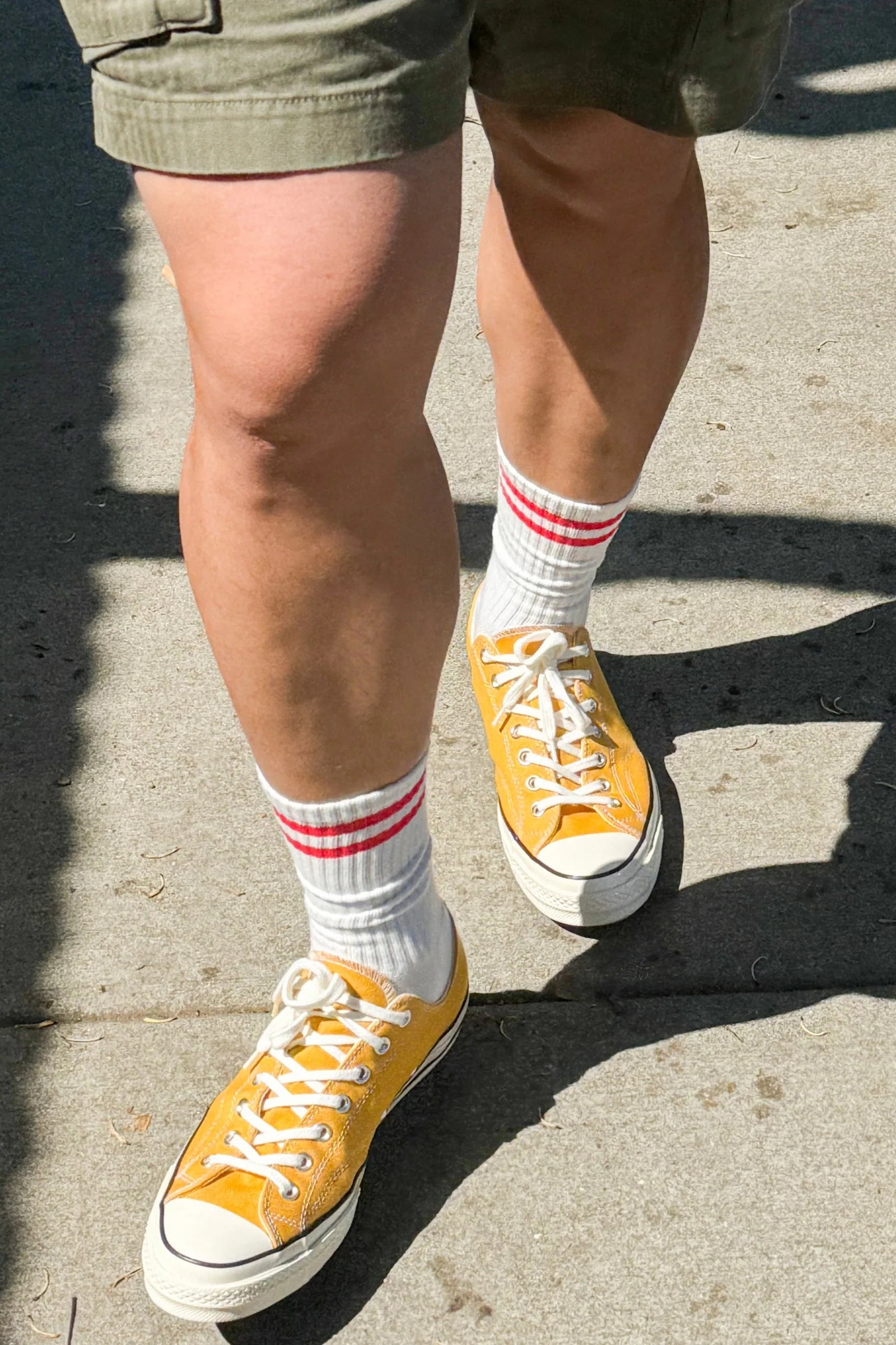Person wearing green shorts, white socks with red stripes and yellow sneakers walking on a sidewalk.