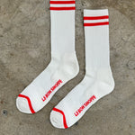 White socks with red stripes and Le Bon Shoppe branding laying on cement floor.