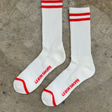 White socks with red stripes and Le Bon Shoppe branding laying on cement floor.