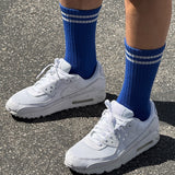 A pair of cobalt blue calf-length socks with white stripes, worn with white sneakers.