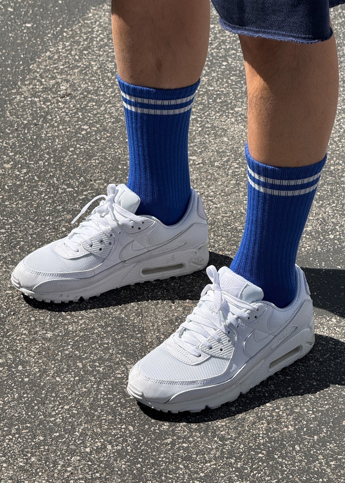 A pair of cobalt blue calf-length socks with white stripes, worn with white sneakers.