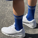 A pair of cobalt blue calf-length socks with white stripes, worn with white sneakers.