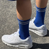 A pair of cobalt blue calf-length socks with white stripes, worn with white sneakers.