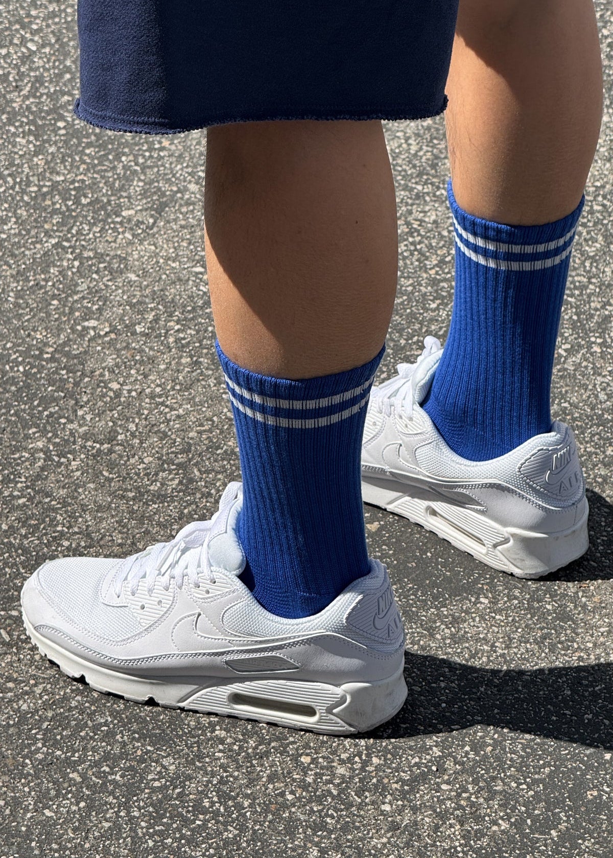 A pair of cobalt blue calf-length socks with white stripes, worn with white sneakers.