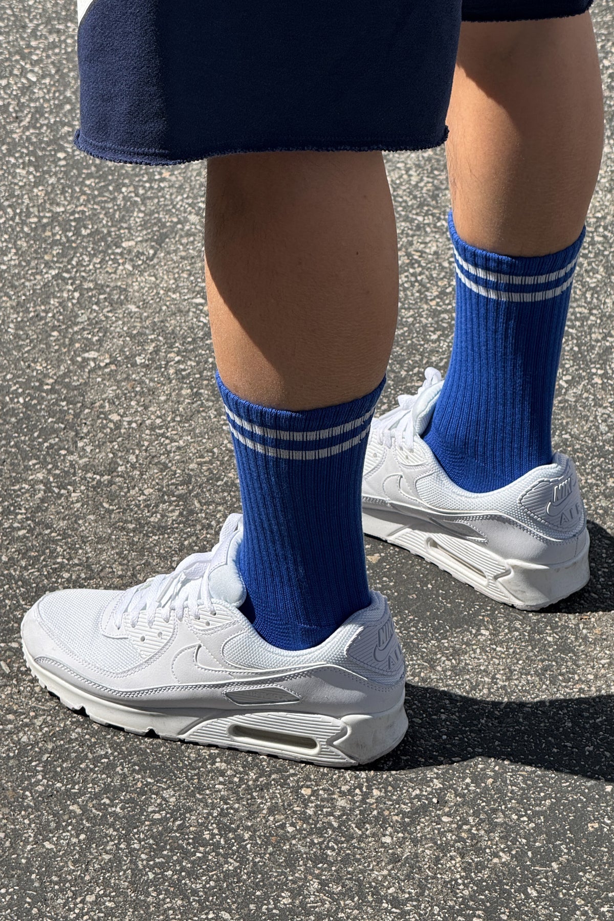 A pair of cobalt blue calf-length socks with white stripes, worn with white sneakers.
