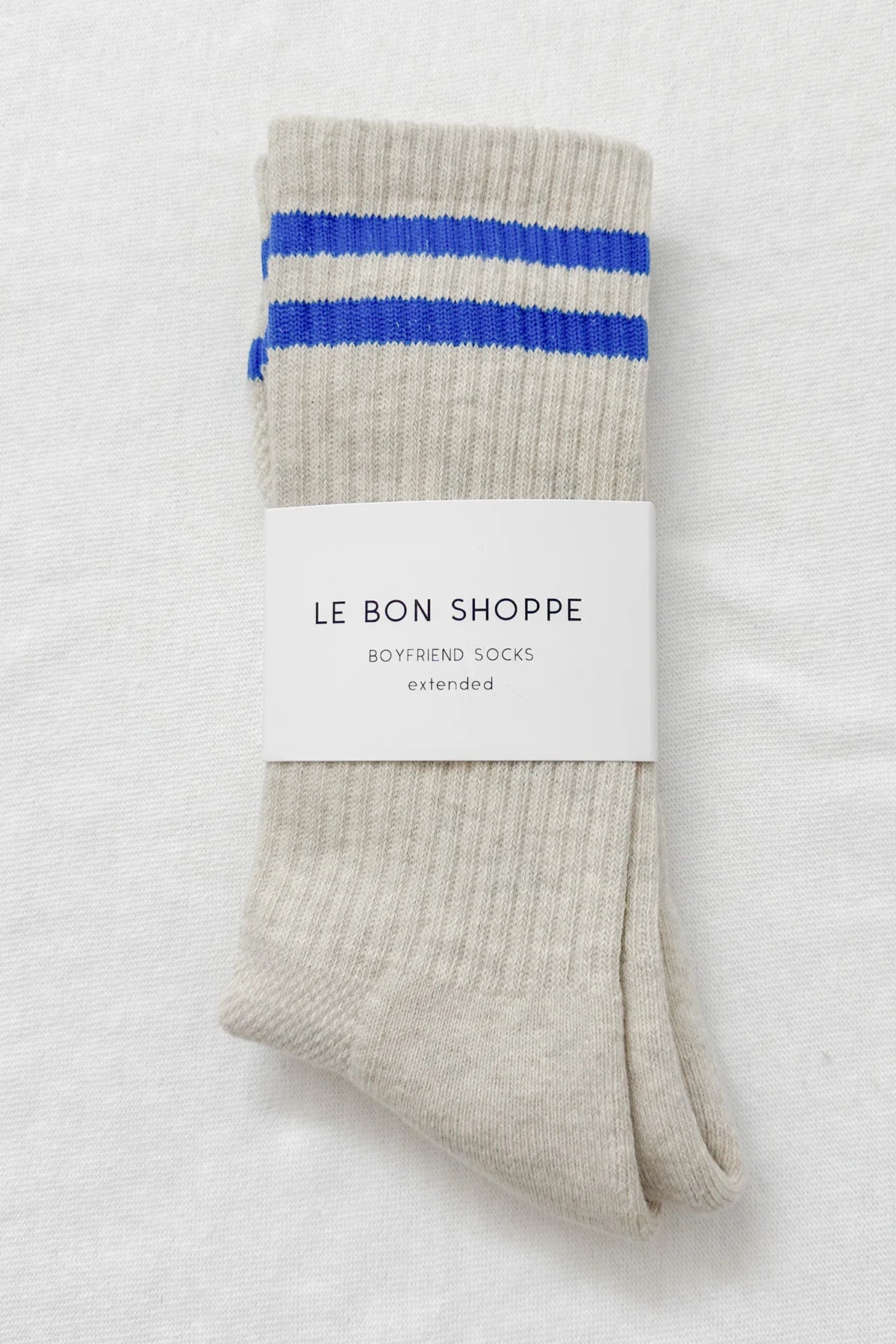 Folded socks with blue stripes and 'Le Bon Shoppe' label on a light gray background