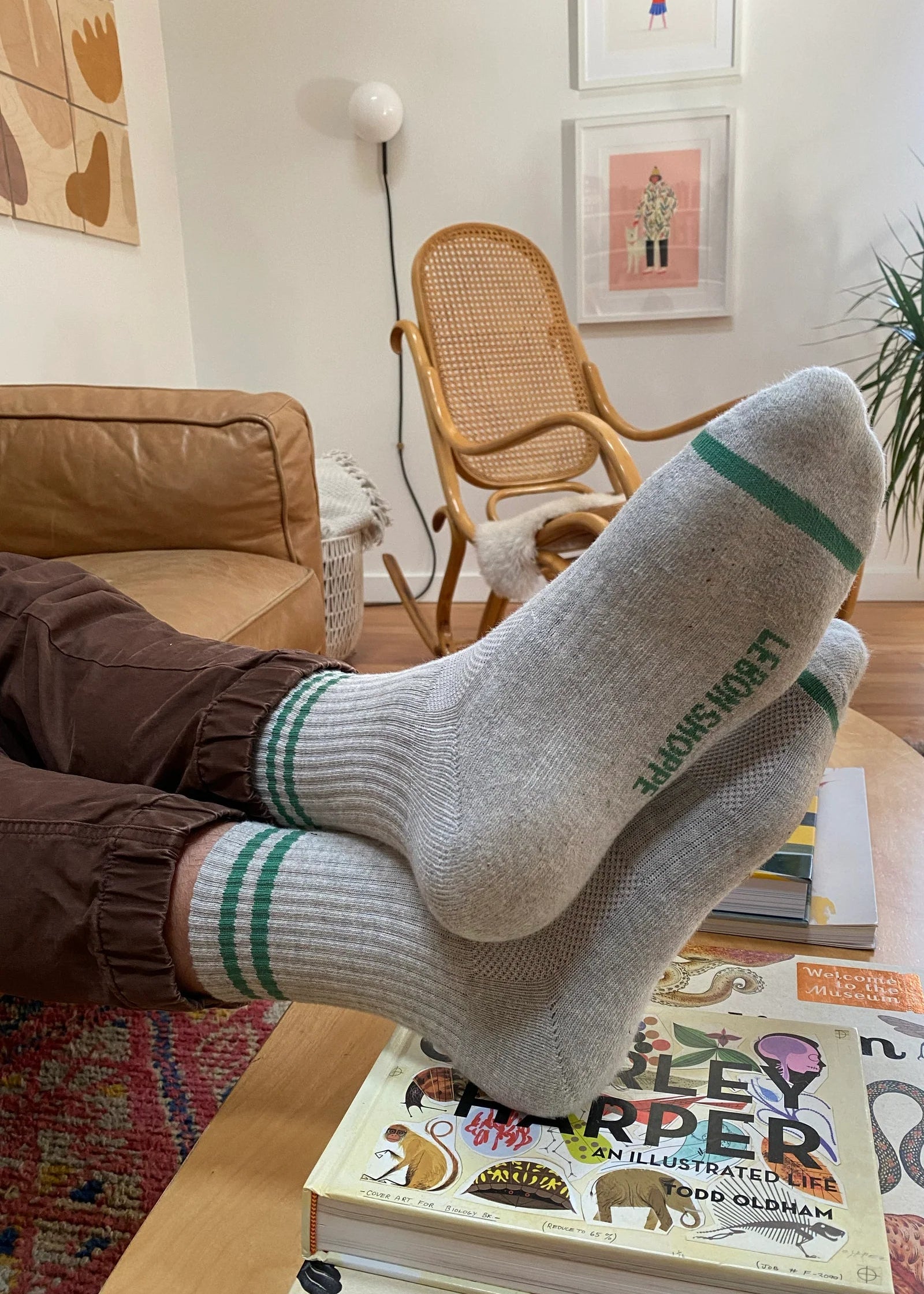 Person wearing socks with a brand logo, sitting on a coffee table with books in a cozy living room.