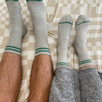 Two pairs of legs wearing gray socks with green accents on a checkered bedspread.