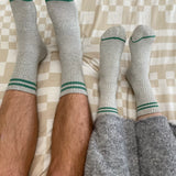 Two pairs of legs wearing gray socks with green accents on a checkered bedspread.