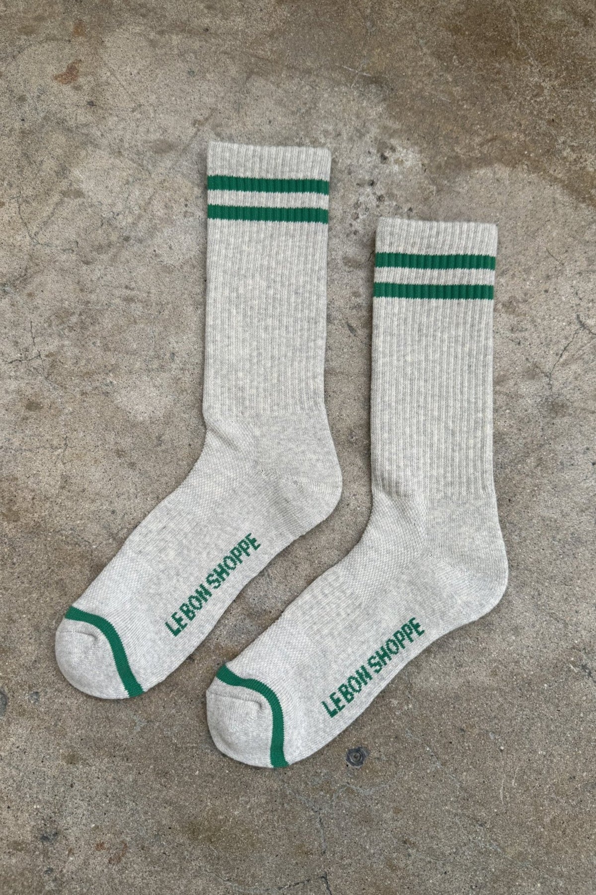 Pair of gray socks with green stripes and text on a concrete surface