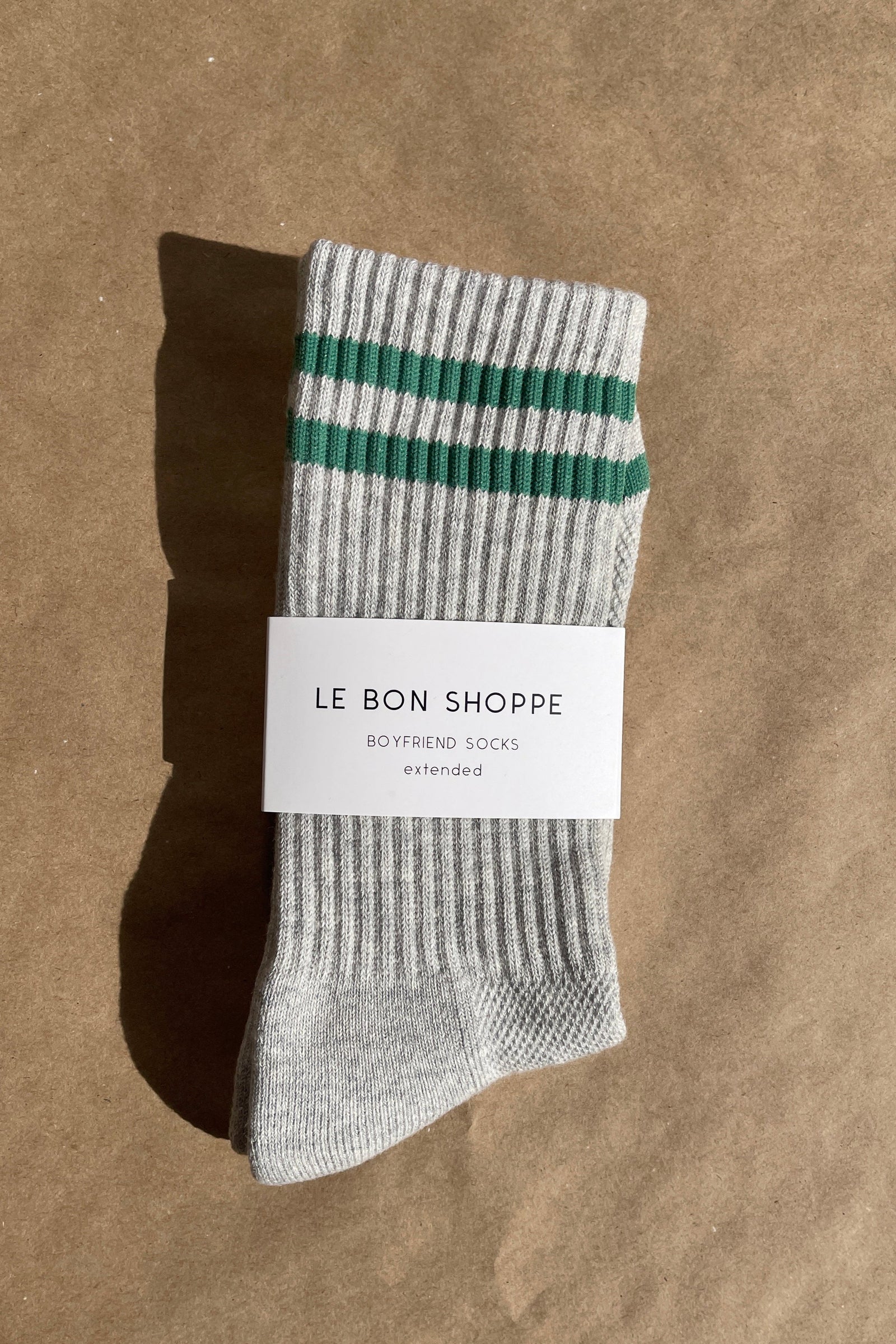 Gray sock with green stripes on a brown background, featuring 'Le Bon Shoppe' label.