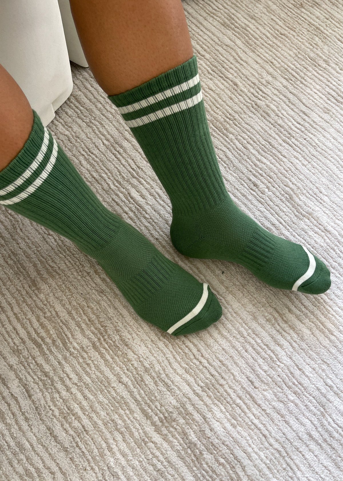 Person wearing green socks with white stripes on carpet floor