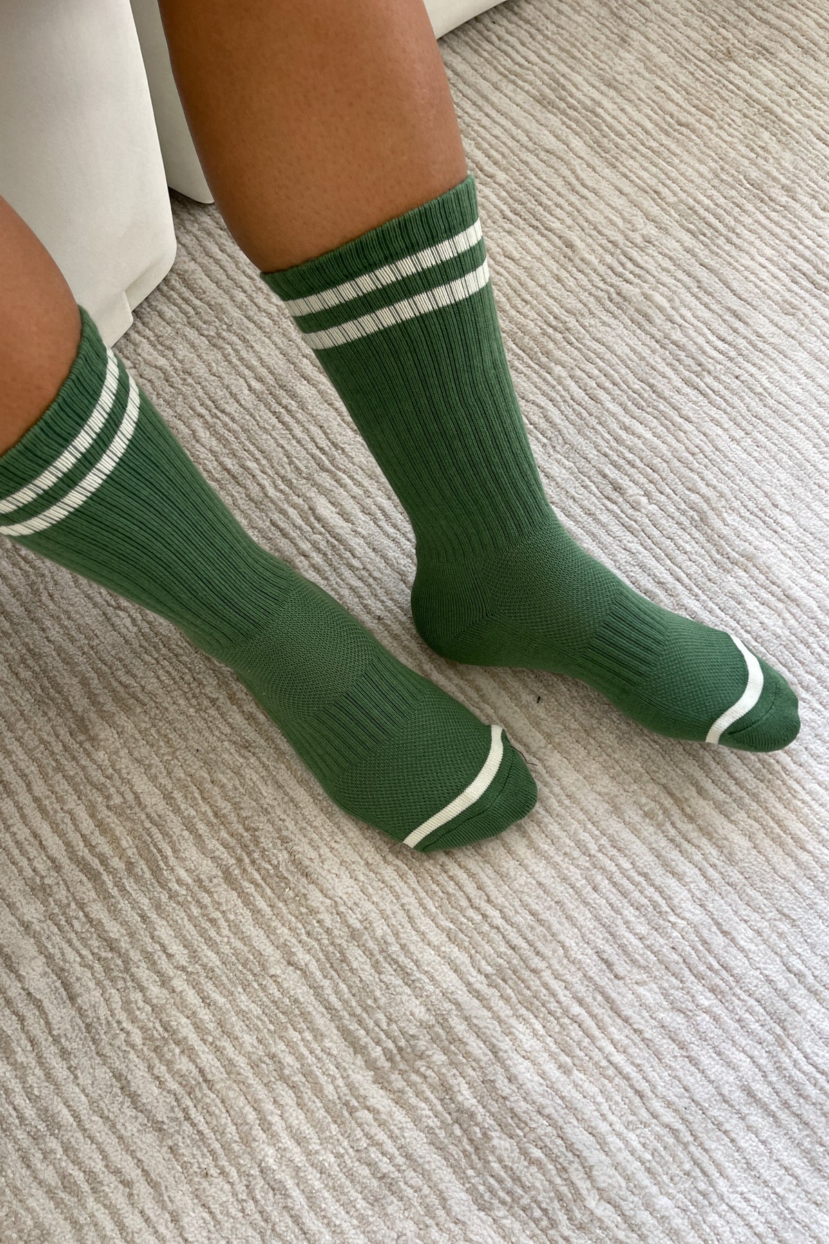 Person wearing green socks with white stripes on carpet floor
